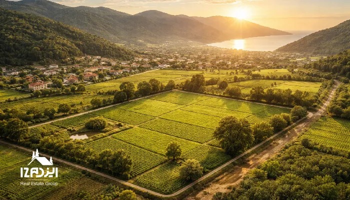 نمای هوایی لنداسکیپ از زمینهای قطعهبندیشده و مزارع سبز در حاشیه یک شهرک کوچک، با جاده دسترسی مشخص و نور طلایی غروب؛ نمادی از زمین قابل رشد برای سرمایهگذاری.